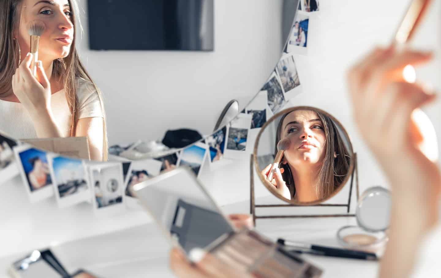 A pregnant woman applies makeup at home in front of a mirror.